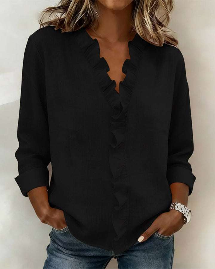  Woman in a relaxed fit blouse with long sleeves and soft ruffle trim.