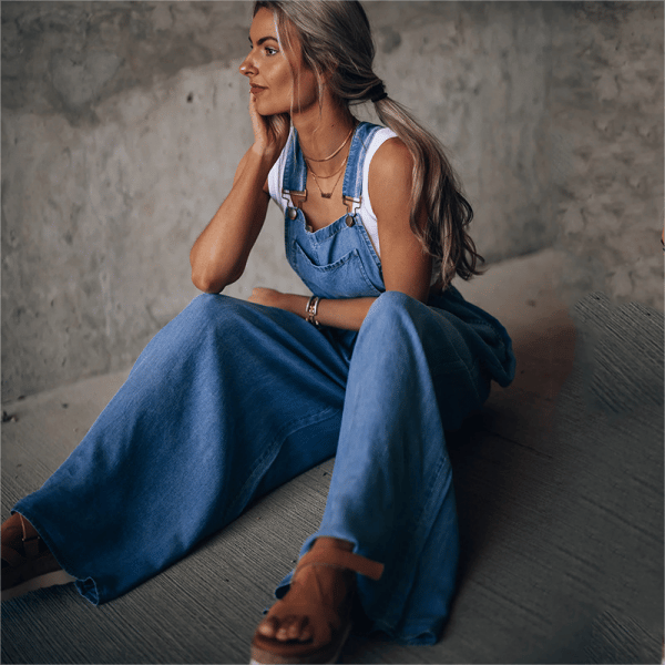 Female model in a bib-front denim jumpsuit on a plain background.