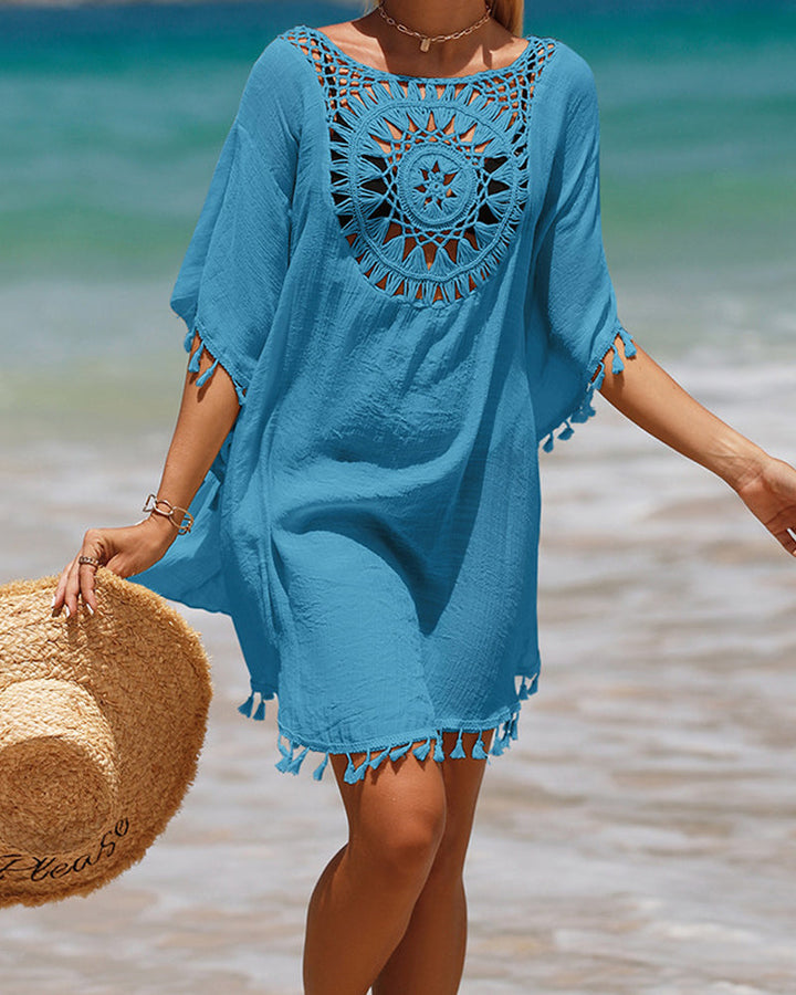 Woman modeling an airy beach cover up with boho pattern and tassel details on a plain background.