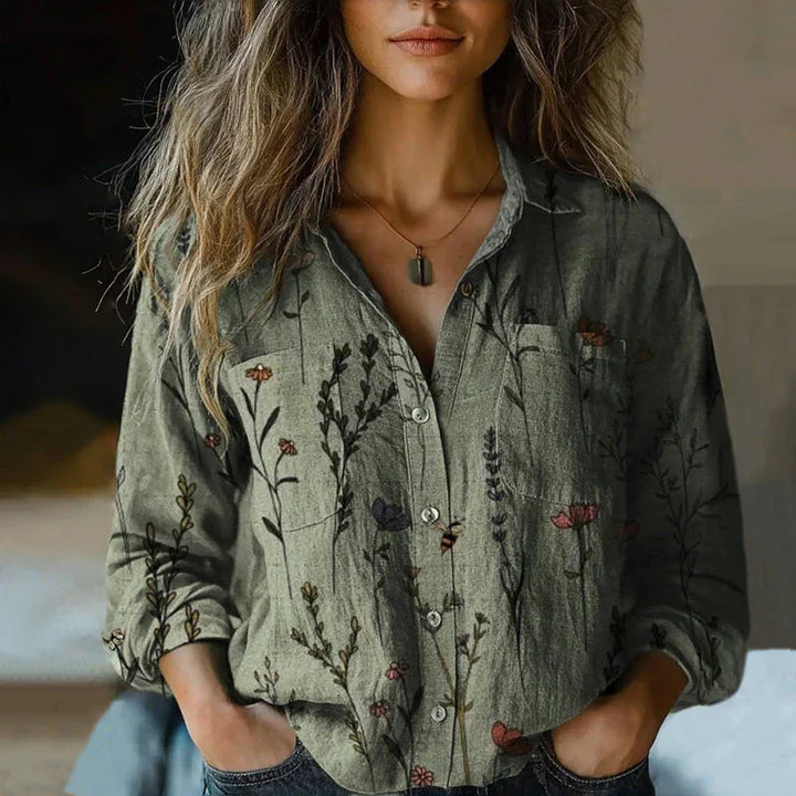  Female modelling a patterned blouse with flowing sleeves on a plain background.
