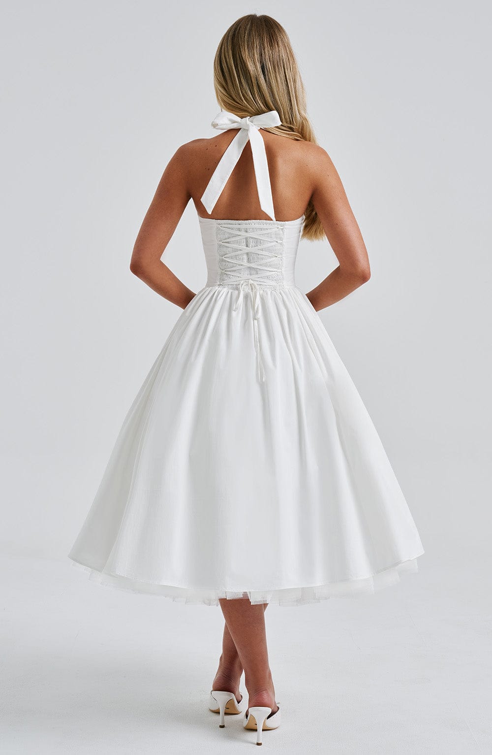 Model in a halter midi dress with soft skirt movement against a plain background.