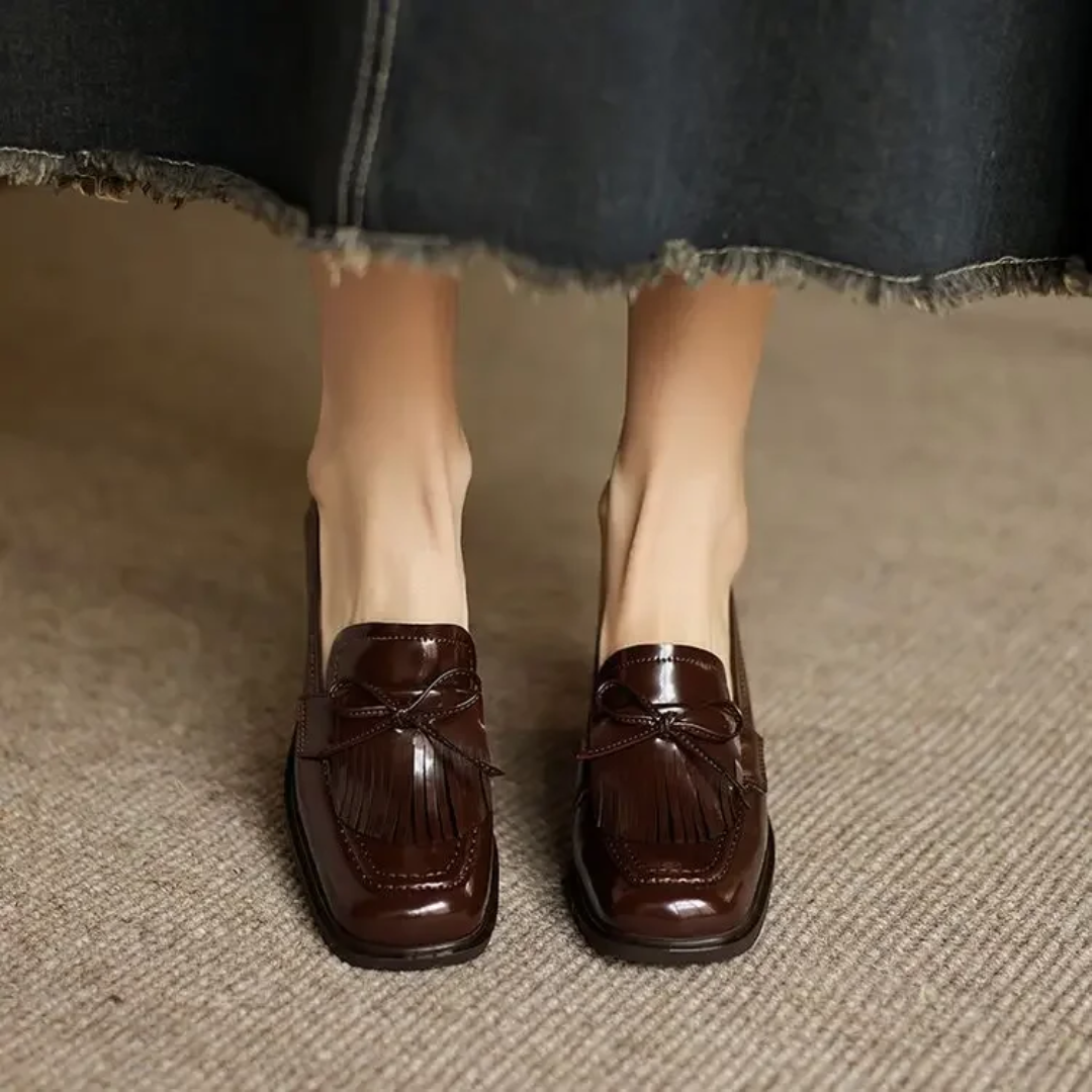 Woman modelling smart tassel loafers with elevated heel on a plain background.