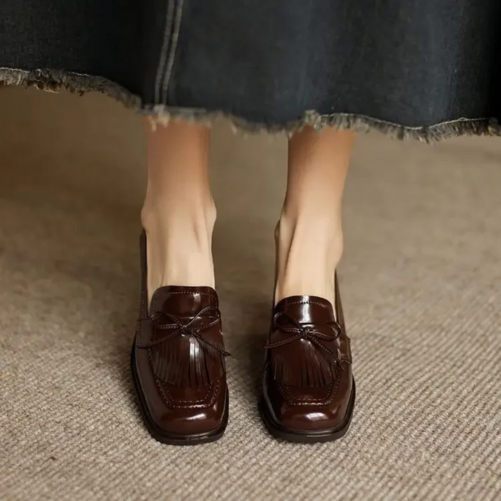 Woman modelling smart tassel loafers with elevated heel on a plain background.