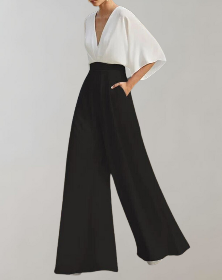 Model in a chic one piece outfit with dramatic sleeves on a plain background.