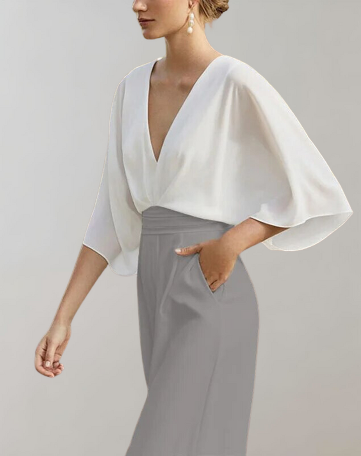 Female model wearing a wide leg evening jumpsuit with a deep V neckline on a plain background.