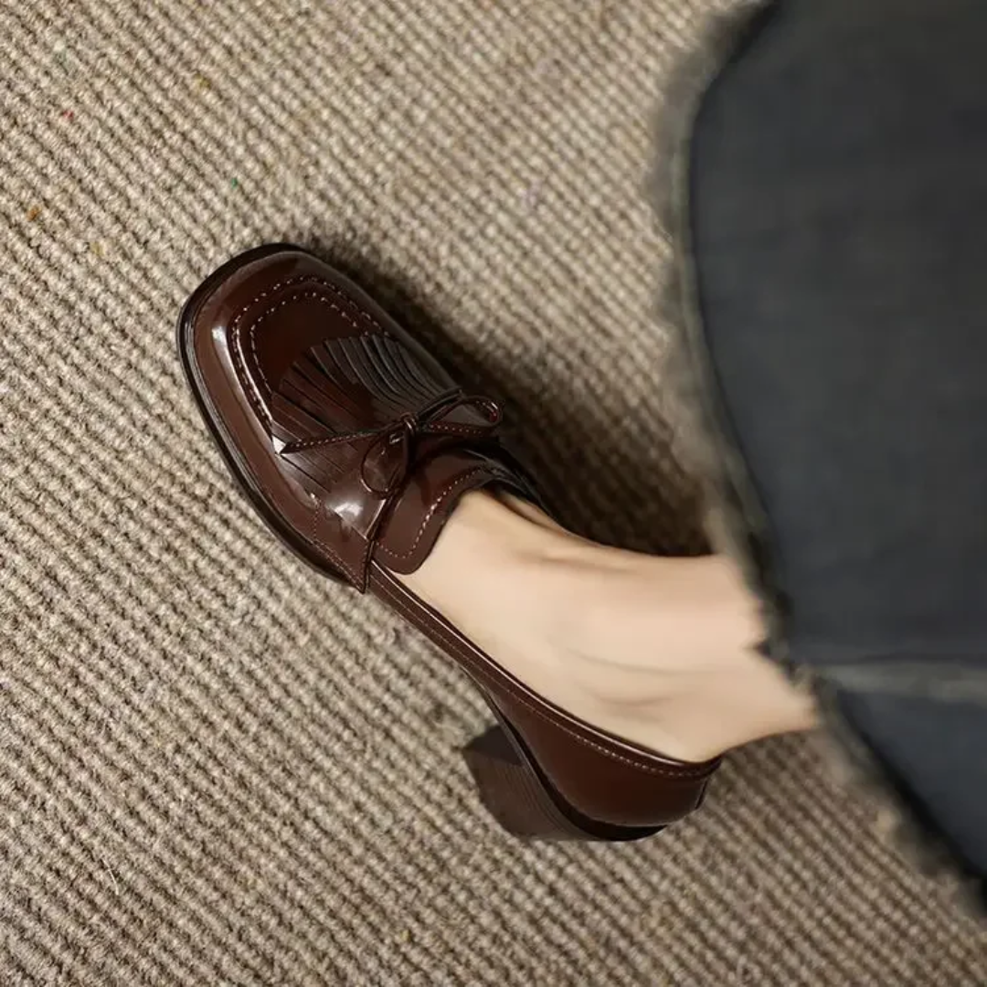 Woman displaying refined tassel heel loafers for smart styling on a plain background.