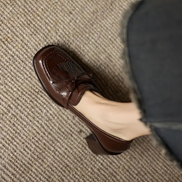 Woman displaying refined tassel heel loafers for smart styling on a plain background.