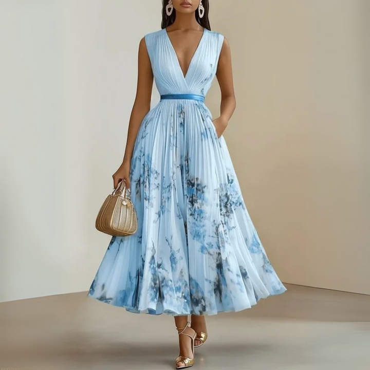 Female wearing a long pleated dress with a V-shaped neckline on a plain background.