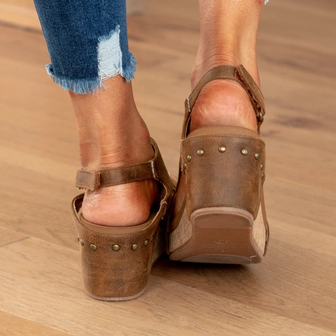 Woman posing in closed-toe wedge footwear on a plain background.