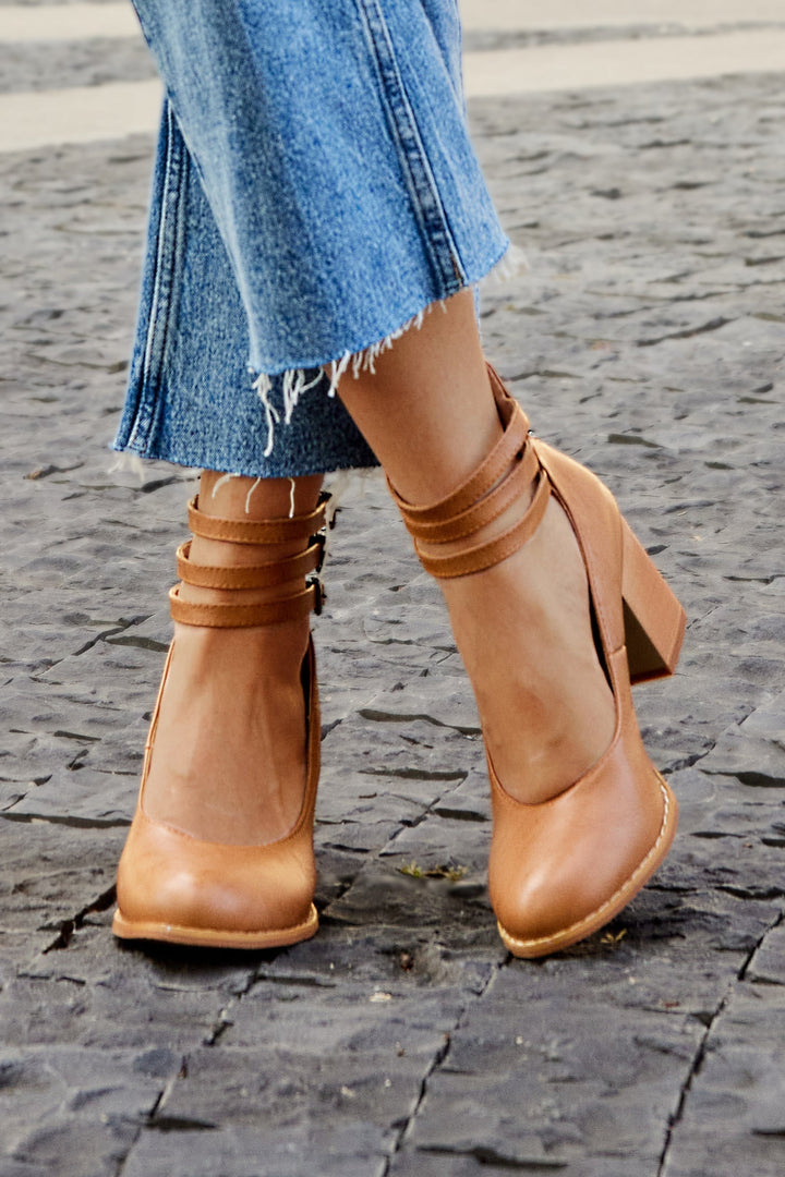 Female wearing open toe heeled sandals with an ankle strap on a plain background.