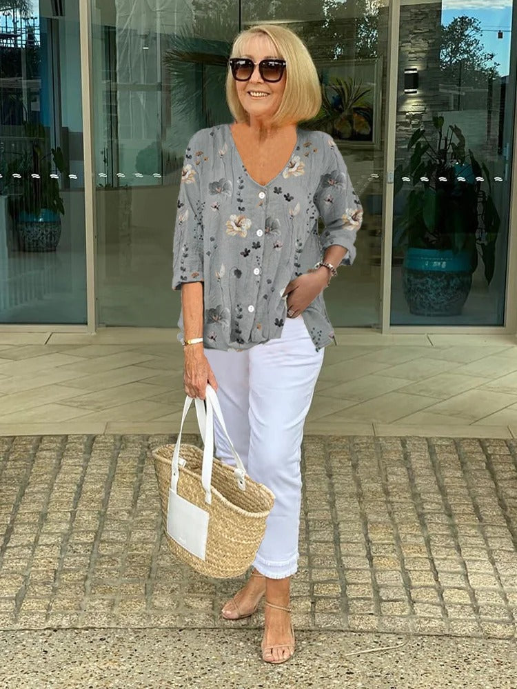 Woman styling a V-neck printed blouse with three-quarter sleeves on a plain background.