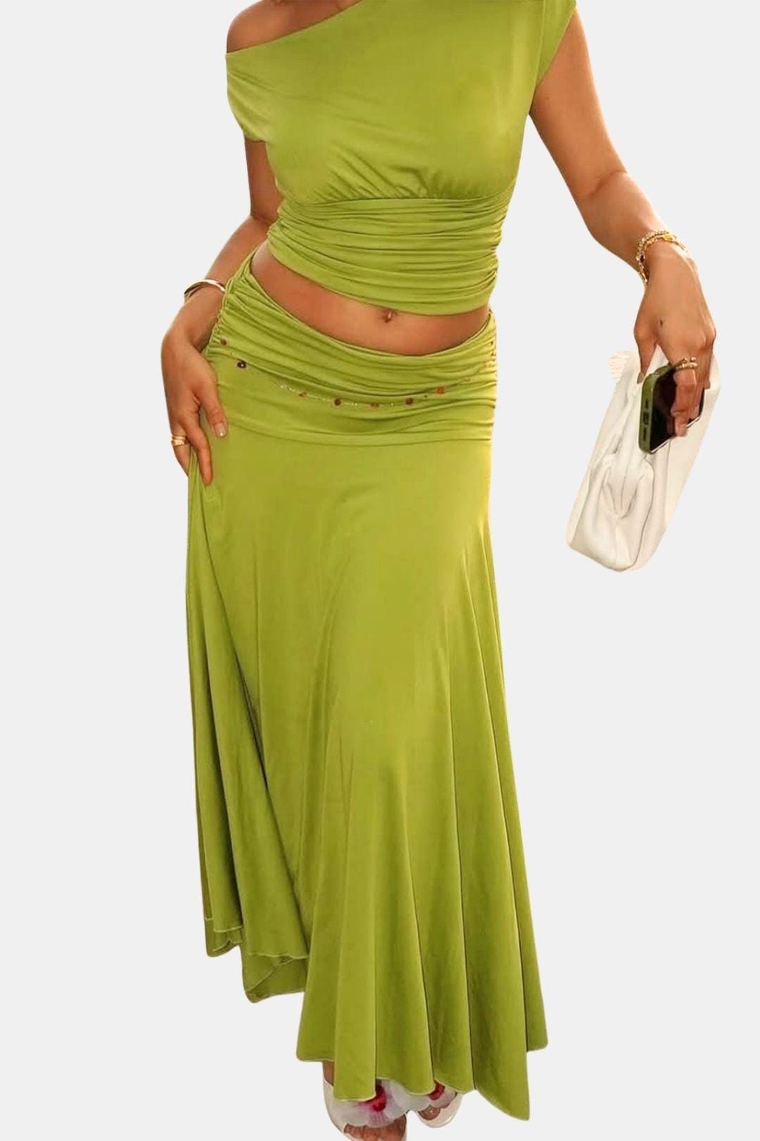 Woman in a green asymmetrical crop top and ruched maxi skirt on a plain background.