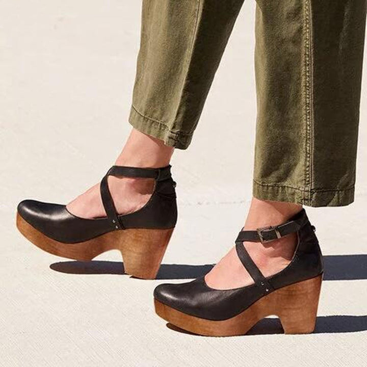 Woman wearing closed toe wedge heels with ankle straps on a plain background.