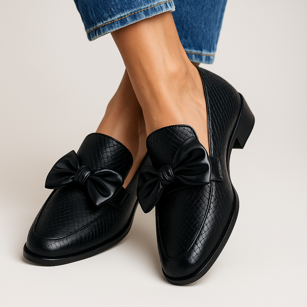 Woman wearing bow loafers on a plain background.