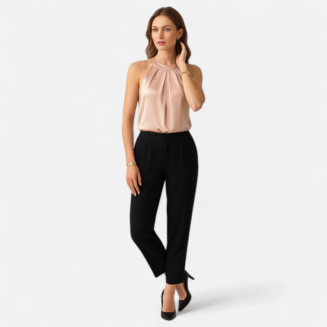 Woman styled in a sleeveless pleated top against a plain background.