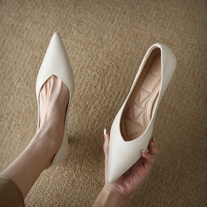 Female model wearing neutral pointed toe dress shoes on a plain background.
