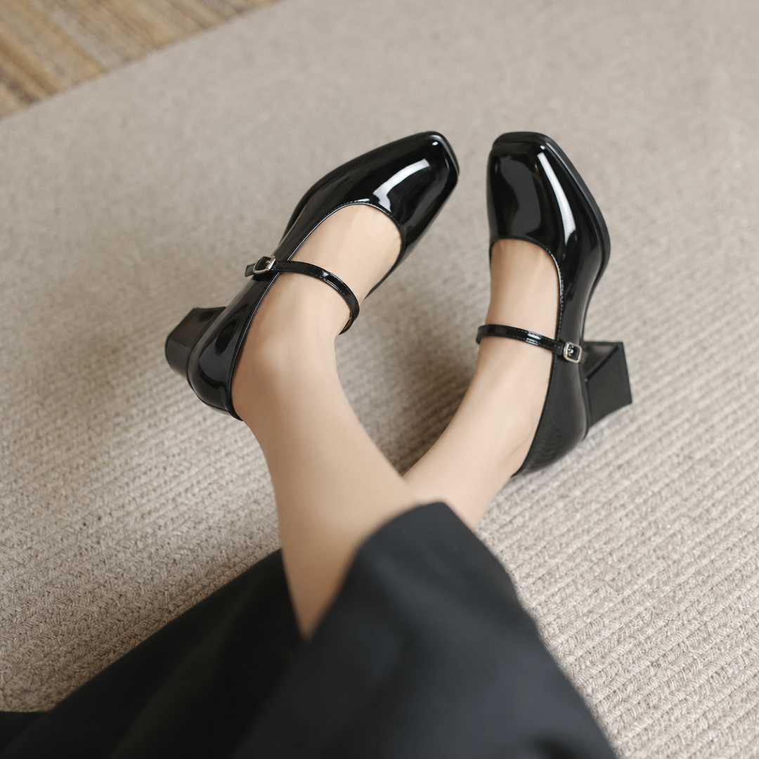 Woman showcasing burgundy square toe block heel pumps on a plain background.