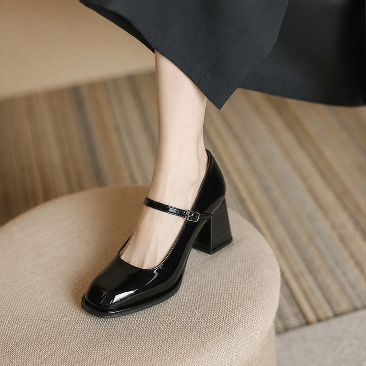 Female wearing black ankle strap block heel pumps on a plain background.