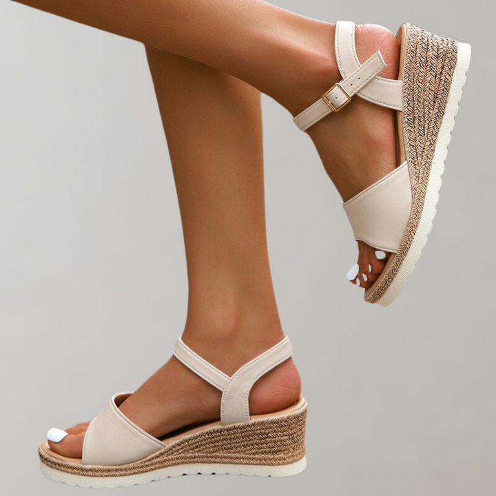 Woman wearing open-toe wedge sandals with adjustable fit on a plain background.