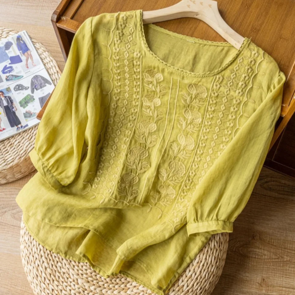 Woman styled in an embroidered short sleeve blouse against a plain background.