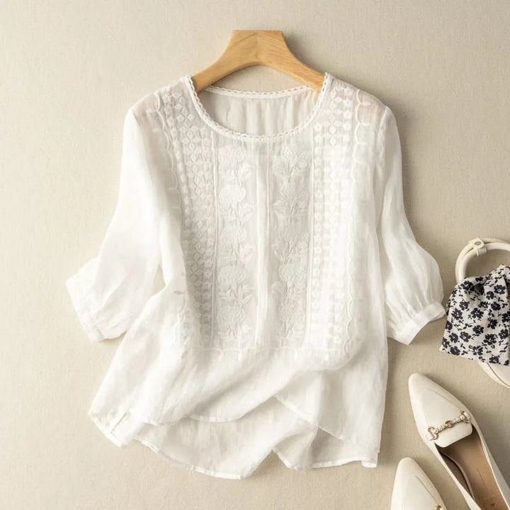 Female model wearing a casual embroidered blouse with a relaxed fit on a plain background.
