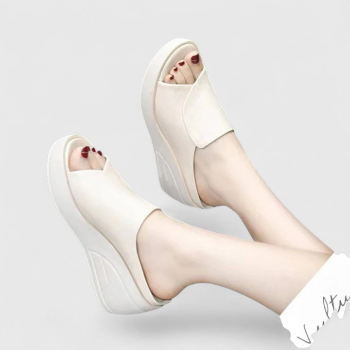 Female model wearing open-toe wedge sandals on a plain background.