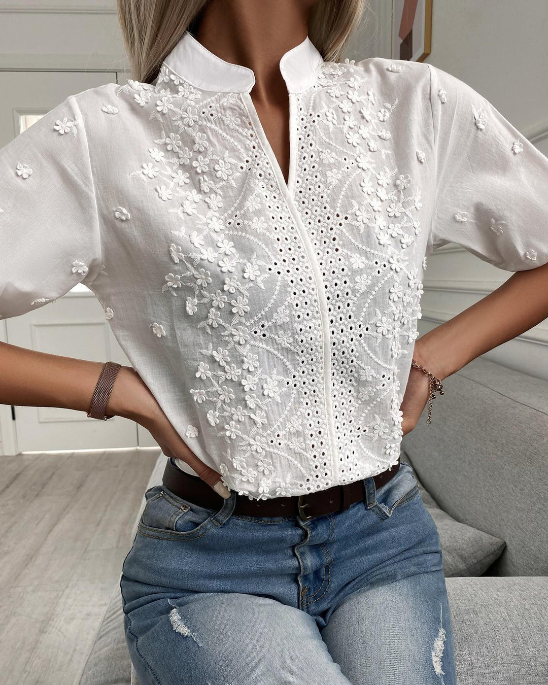 Woman wearing an embroidered button front blouse against a plain background.
