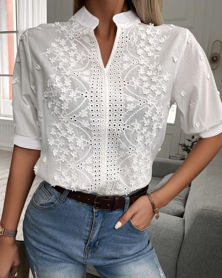 Female model in a floral embroidered blouse on a plain background.