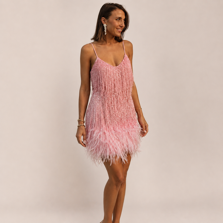 Female model wearing an evening mini dress with feather accents on a plain background.