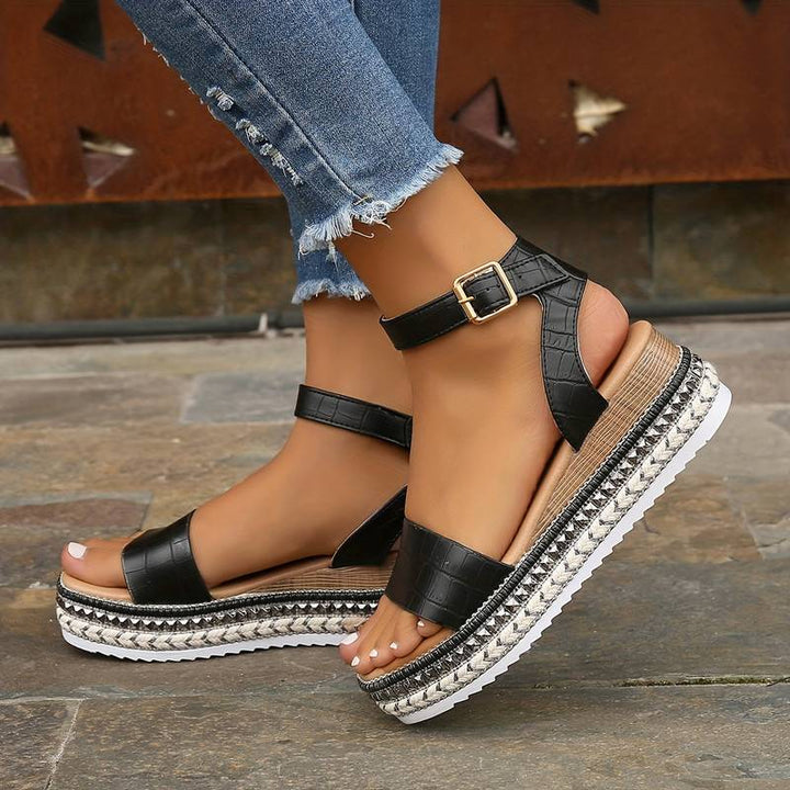 Woman posing in open toe ankle strap sandals on a plain background.
