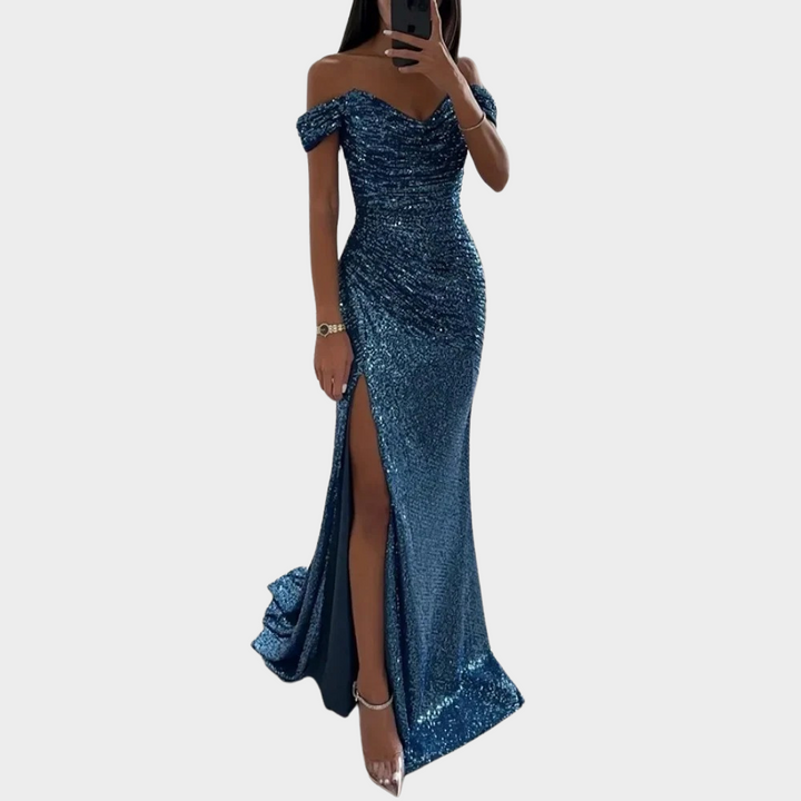 Female model wearing an open shoulder evening dress with a front slit on a plain background.