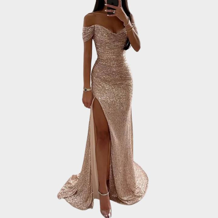Woman wearing a black evening dress with fitted shape and front slit on a plain background.
