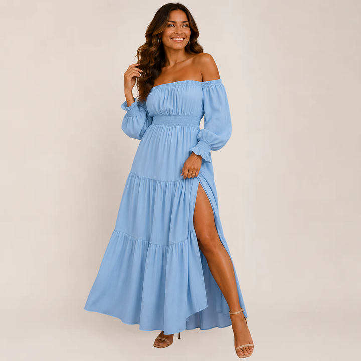 Female in a relaxed off-shoulder summer dress with soft flowing layers on a plain background.
