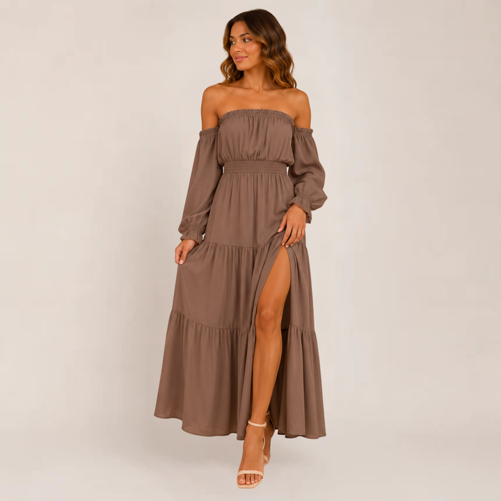 Woman posing in a flowy off-shoulder dress with layered tiers on a plain background.