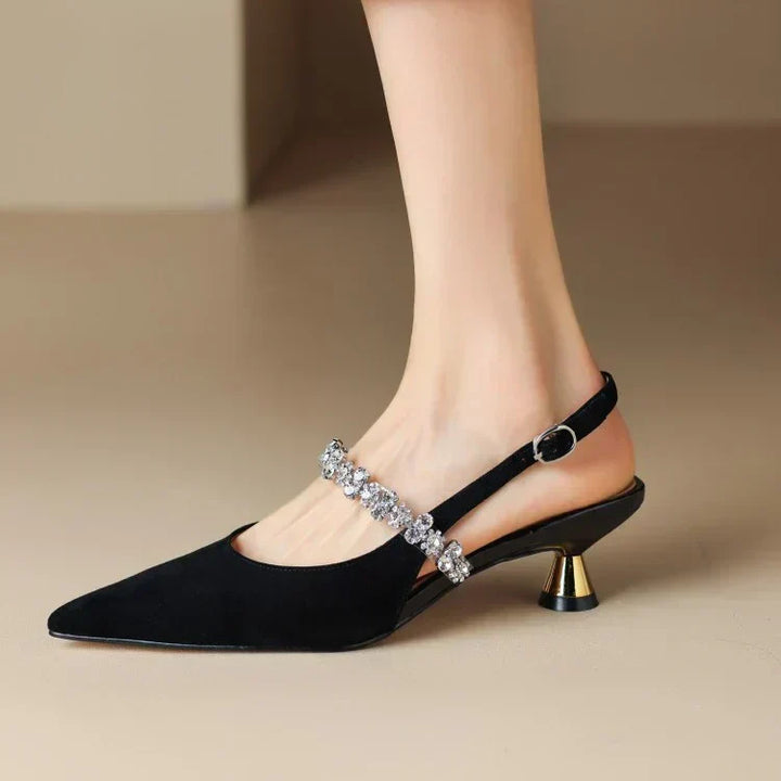 Woman styling slingback heels with shimmering strap detail on a plain background.