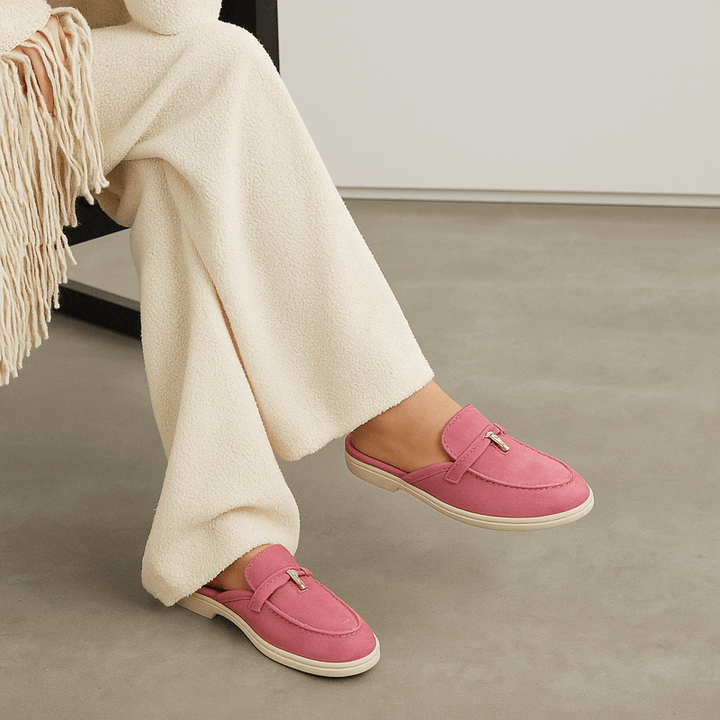 Female model wearing backless mule shoes on a plain background.