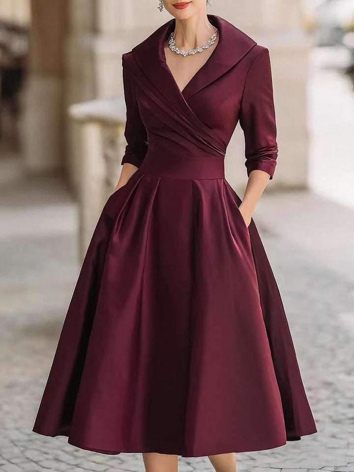 Female model in a dressy midi dress with full skirt and waist detail on a plain background.