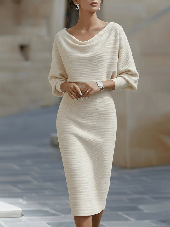 Woman in a white long sleeve midi dress with draped neckline on a plain background.