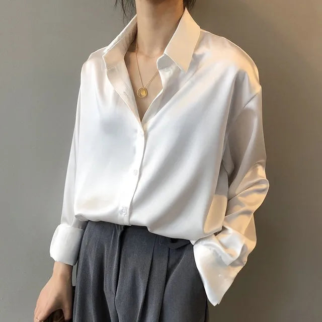  Woman in a smooth satin blouse featuring a classic button-front design on a plain background.