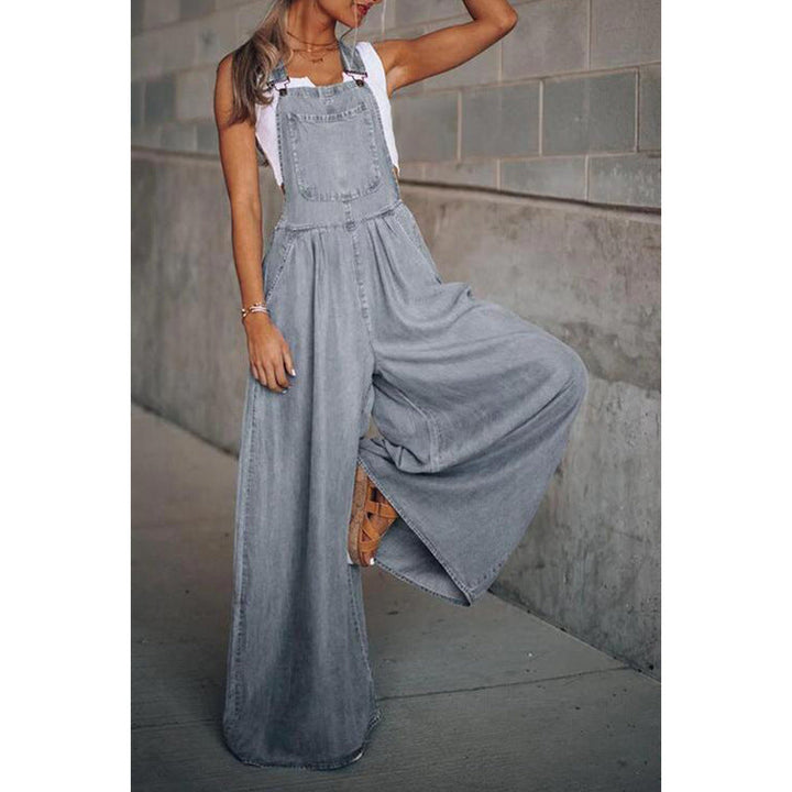 Woman posing in a casual denim overall jumpsuit on a plain background.