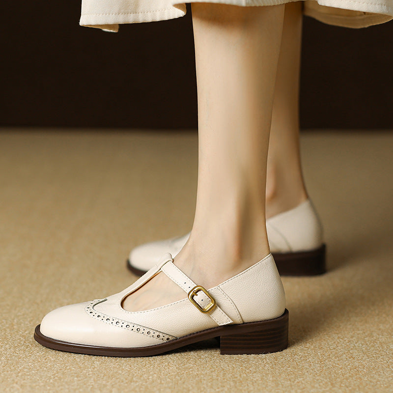T-strap Mary Jane shoe with brogue detailing on a plain background.
