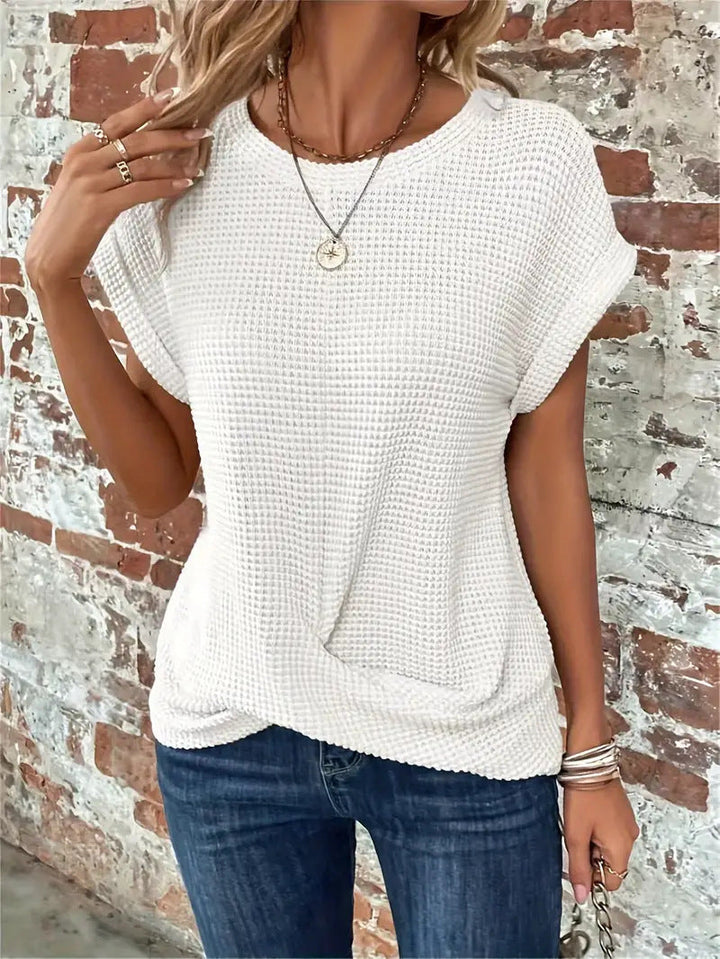 Woman wearing a textured waffle knit top with rolled sleeves against a plain background.