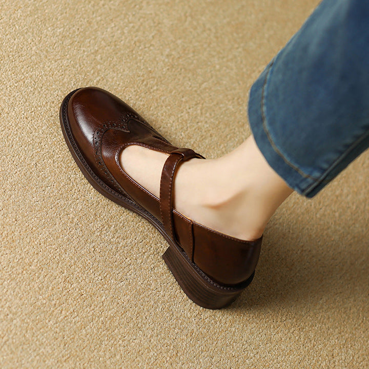 Vintage-inspired Mary Jane shoe with buckle strap and low block heel on a plain background.