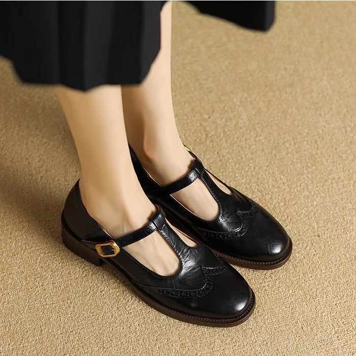Women’s T-bar shoe with wingtip detail and closed toe on a plain background.