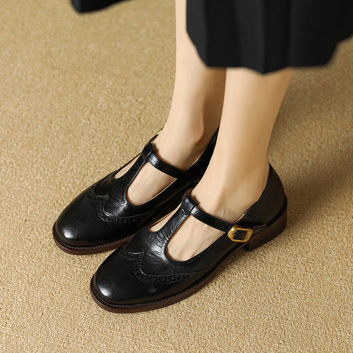 Low heel T-strap shoe with buckle closure on a plain background.