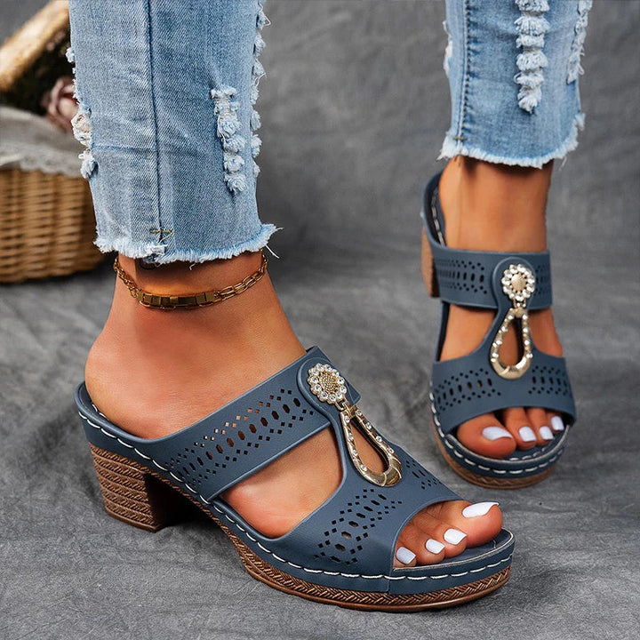 Woman showing wedge sandals with decorative detail on a plain background.