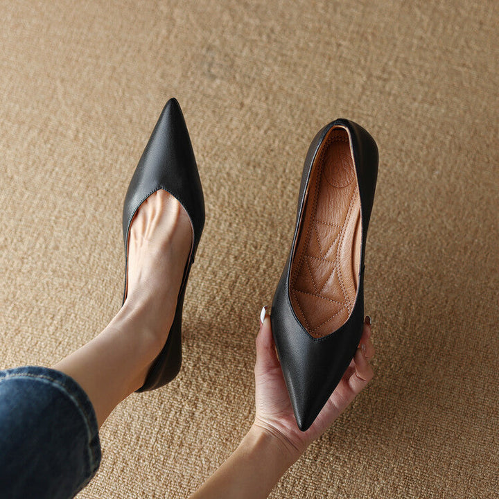 Female model wearing low flared heel pointed pumps on a plain background.