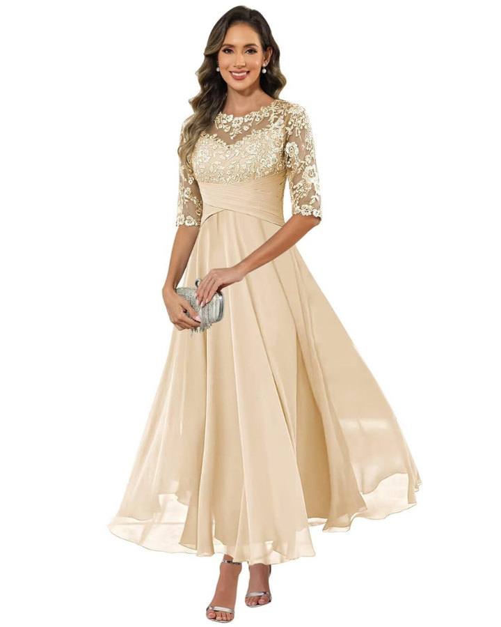 Model in a lace detail evening dress with flowing skirt on a plain background.