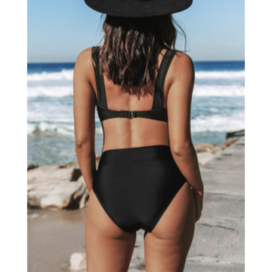 Female posing in a sleeveless one-piece swimsuit with a beach background.