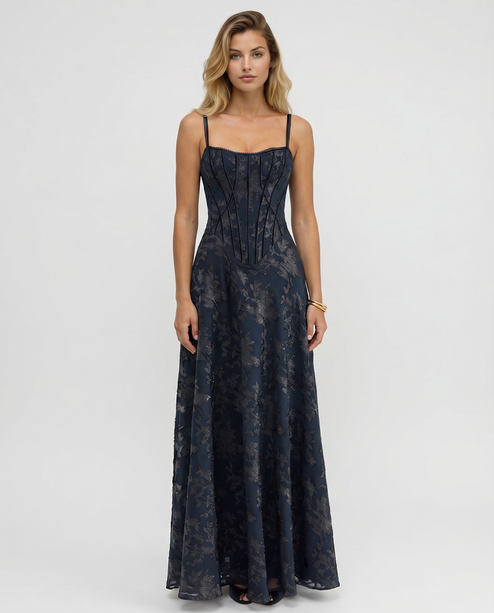 Woman wearing a maxi dress with a structured bodice and flowing skirt against a plain background.